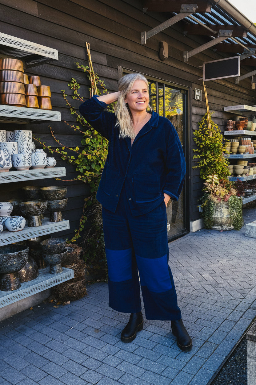 Woman in a blue outfit standing in front of shelves with ceramic items.